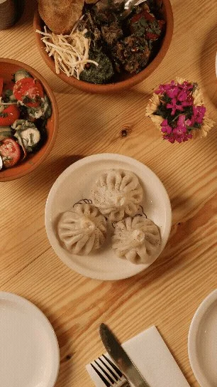 Three khinkali on a plate surrounded by Georgian dishes at Chama Mama