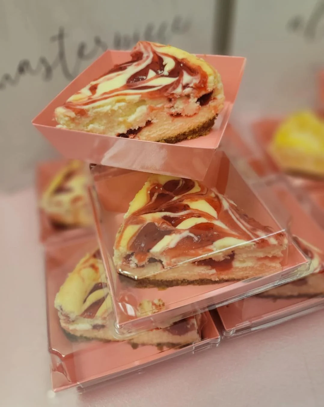 Slices of marbled cheesecake with swirls of red and white in pink containers.