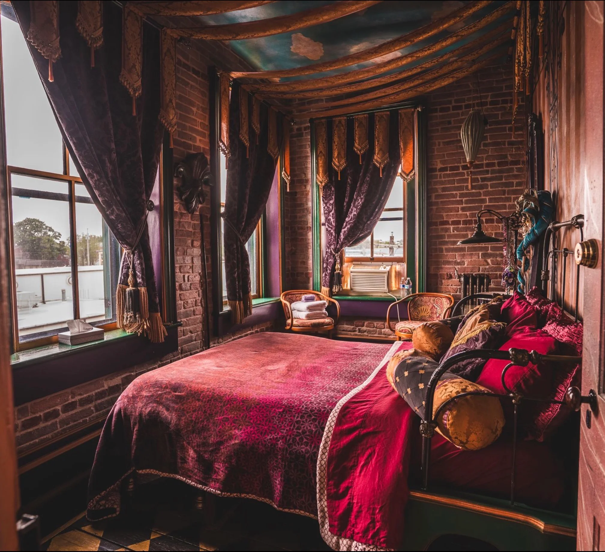 Cozy bedroom with rich fabrics and large windows, featuring a vintage bed.