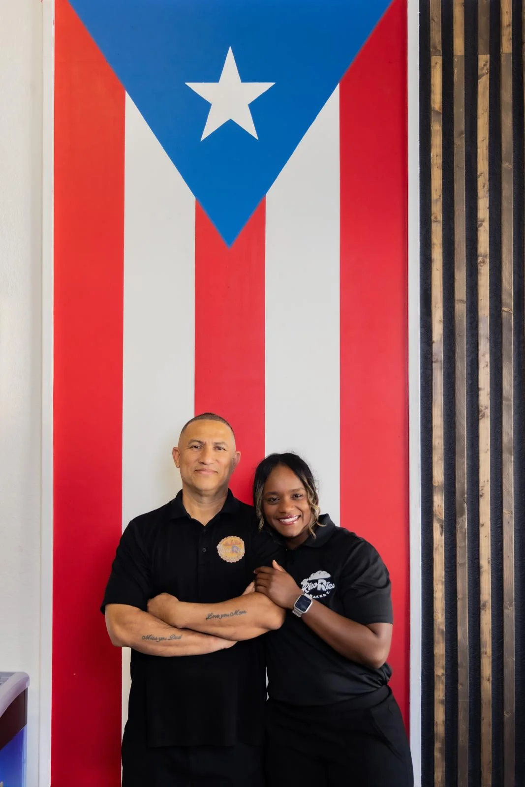 Restaurant owners posing in front of a Puerto Rican flag mural