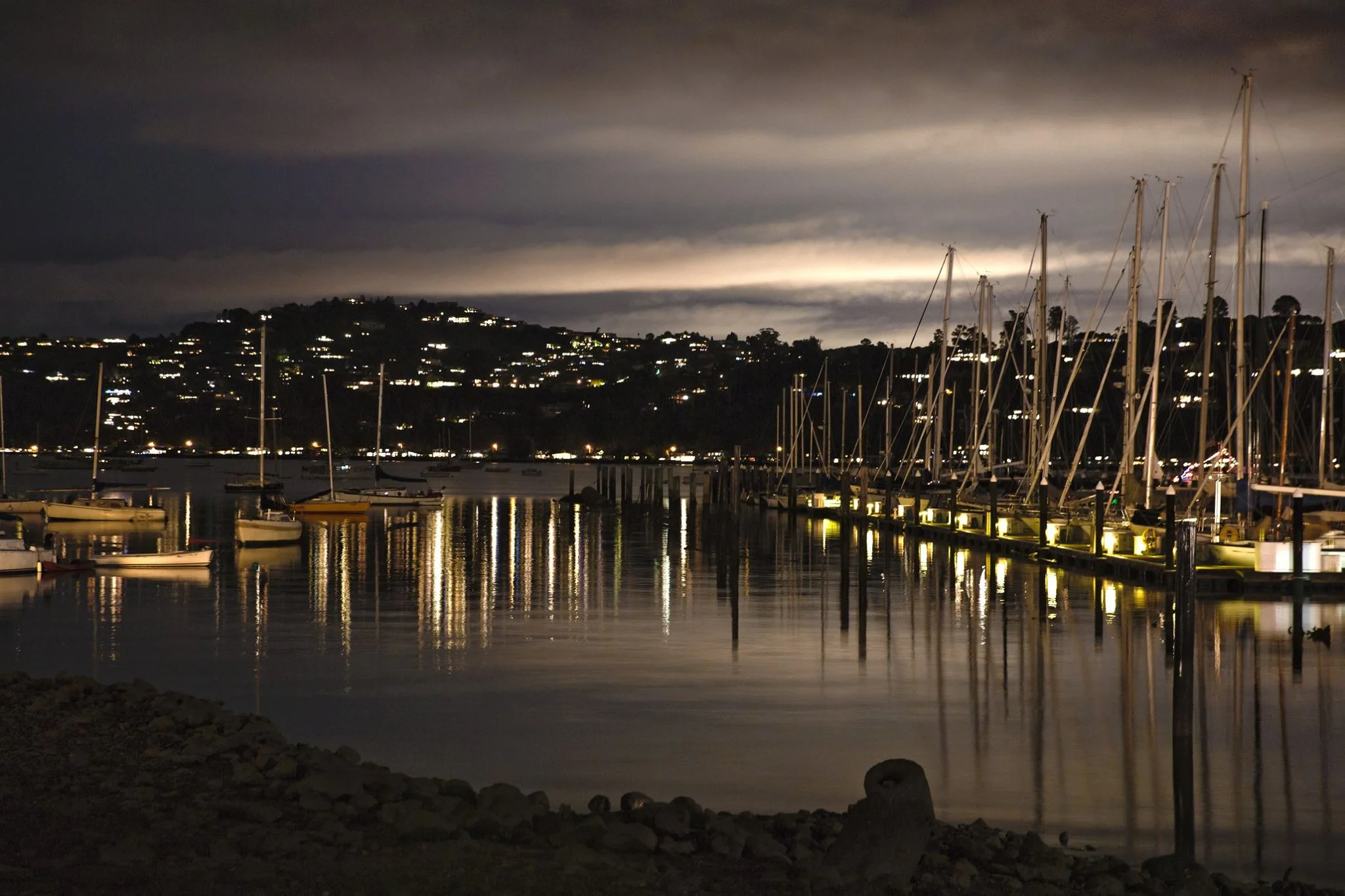The bay at night with lights from the moored boats shining on the calm water