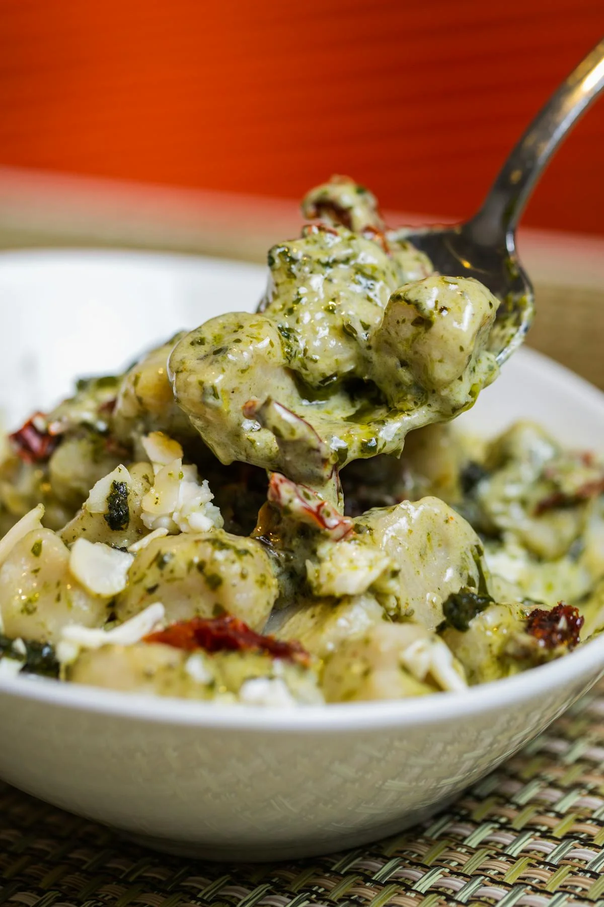 Creamy pesto gnocchi with sun-dried tomatoes and cheese in a bowl.