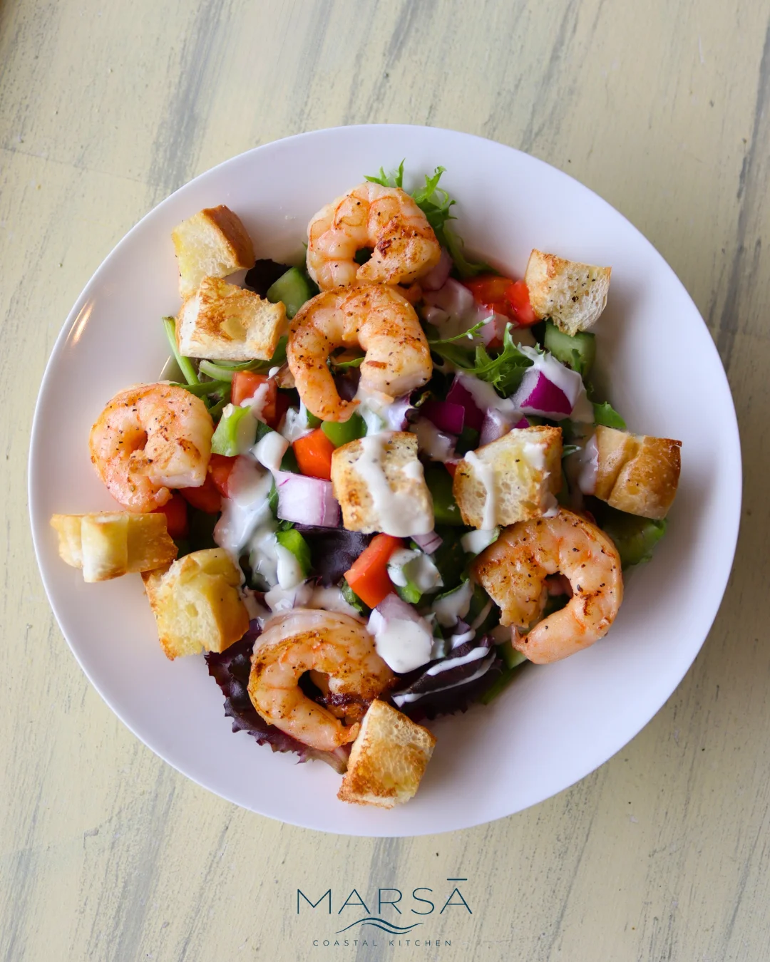A vibrant shrimp salad topped with fresh vegetables and dressing, served on a white plate.