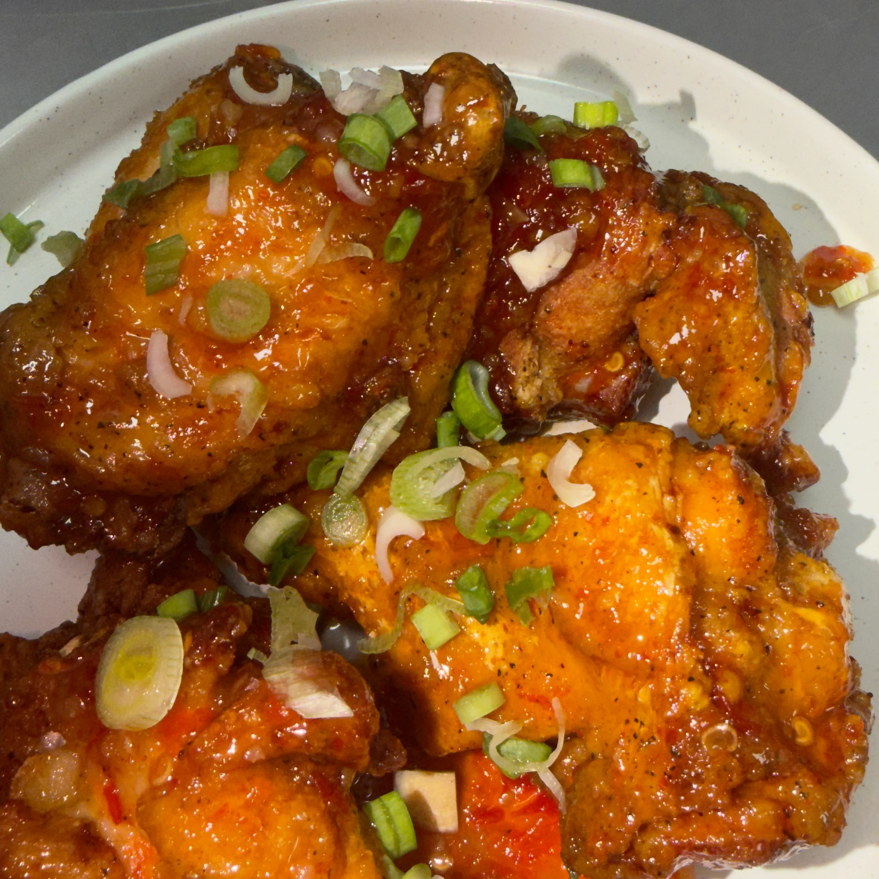Pieces of crispy chicken coated in a spicy glaze, garnished with chopped green onions and white onions.