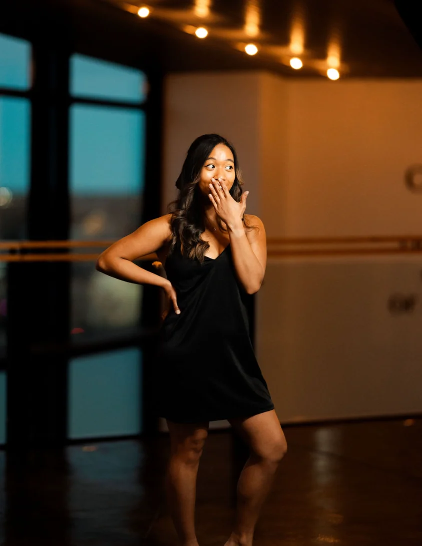 Woman in a black dress posing playfully indoors