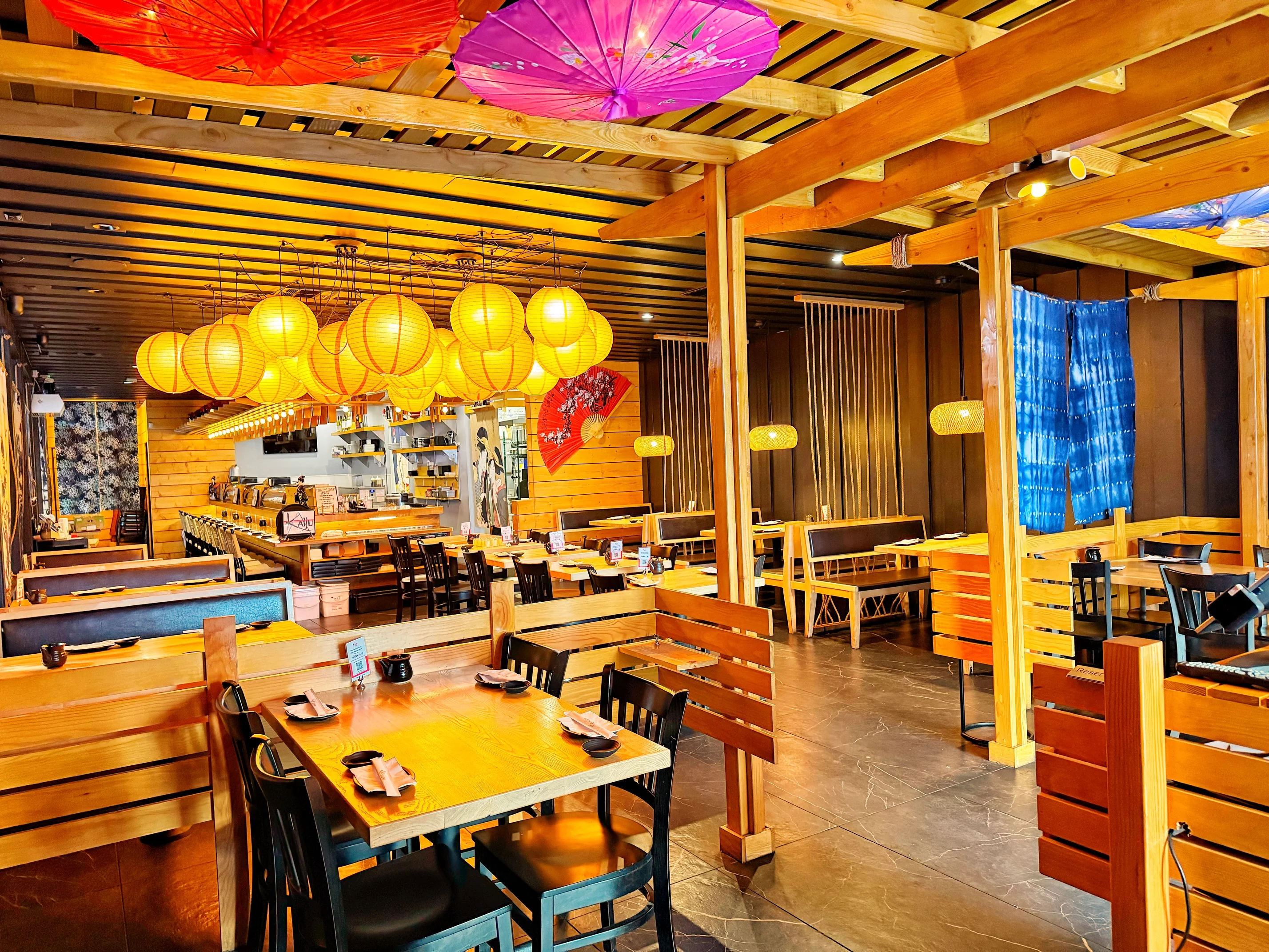 A spacious restaurant interior adorned with overhead lanterns and decorative umbrellas, showcasing wooden furniture and a cozy atmosphere.