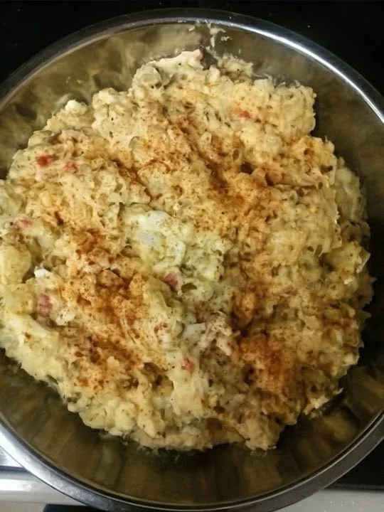 A bowl of creamy potato salad, garnished with paprika and featuring a mix of potatoes and other ingredients.