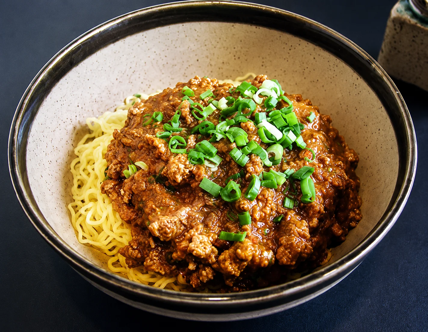 Bowl of spicy noodles topped with savory minced meat sauce and chopped green onions.