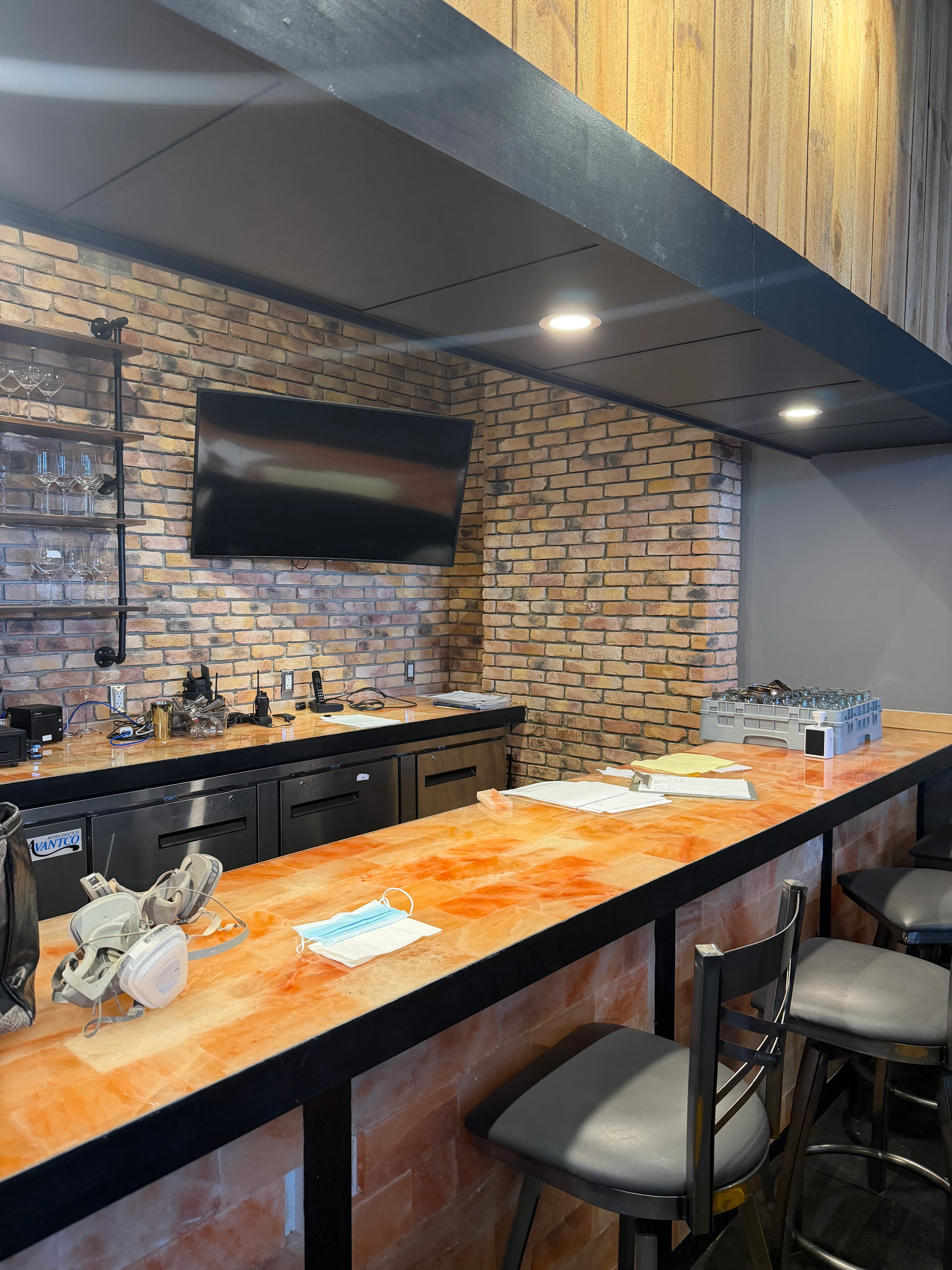 A modern bar area featuring a saltstone countertop, black cabinetry, and a brick wall, complete with a flat-screen TV on display.