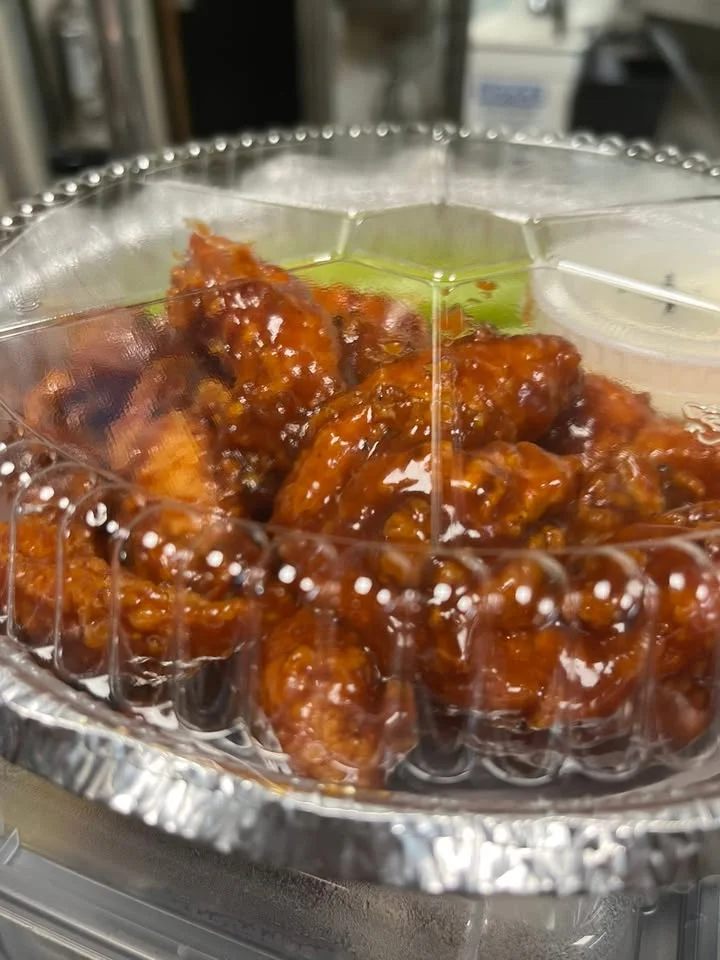 A close-up of sticky glazed chicken pieces in a transparent container, showcasing their shiny appearance.