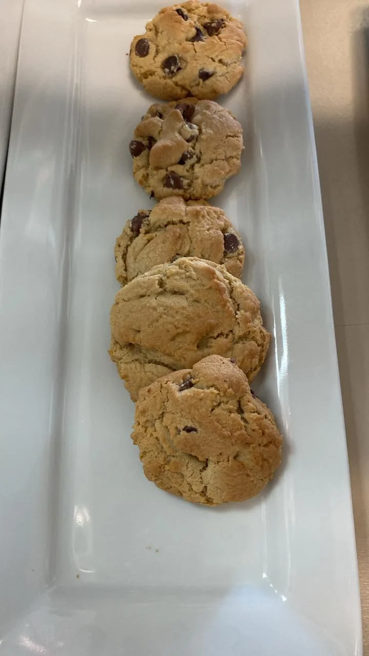 A long white plate holding a line of freshly baked chocolate chip cookies. The cookies are soft and slightly round.