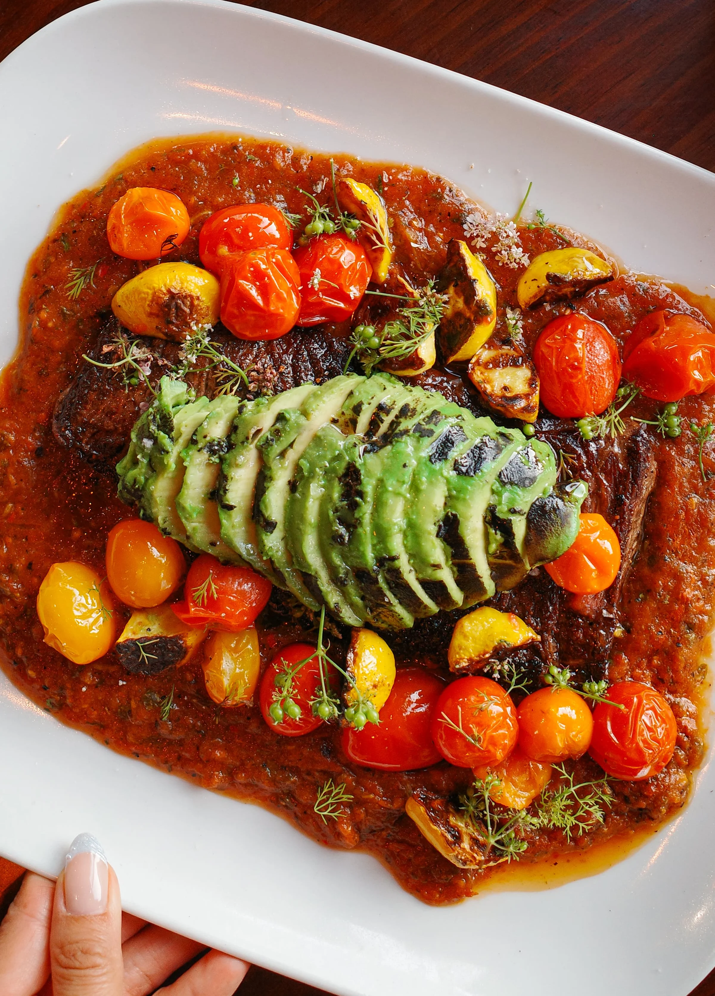 Grilled steak with avocado and cherry tomatoes in a savory sauce