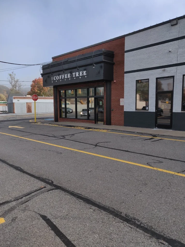 Street view of a brick building with a black sign reading "Coffee Tree Roasters". The scene includes a stop sign and autumn trees in the background.