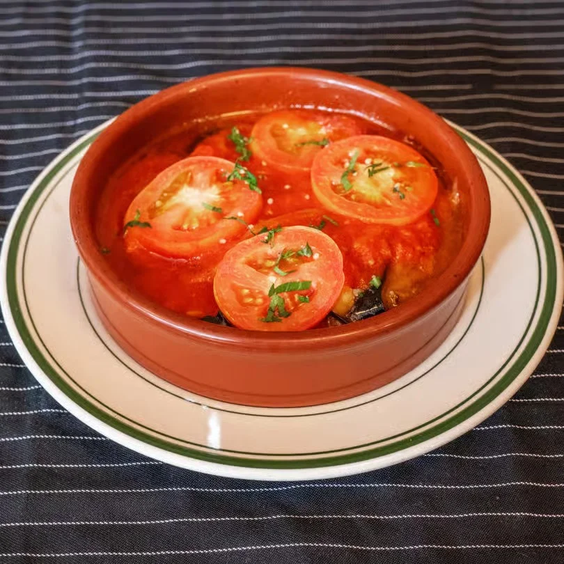 Baked dish with tomatoes and herbs in a clay pot on a plate.