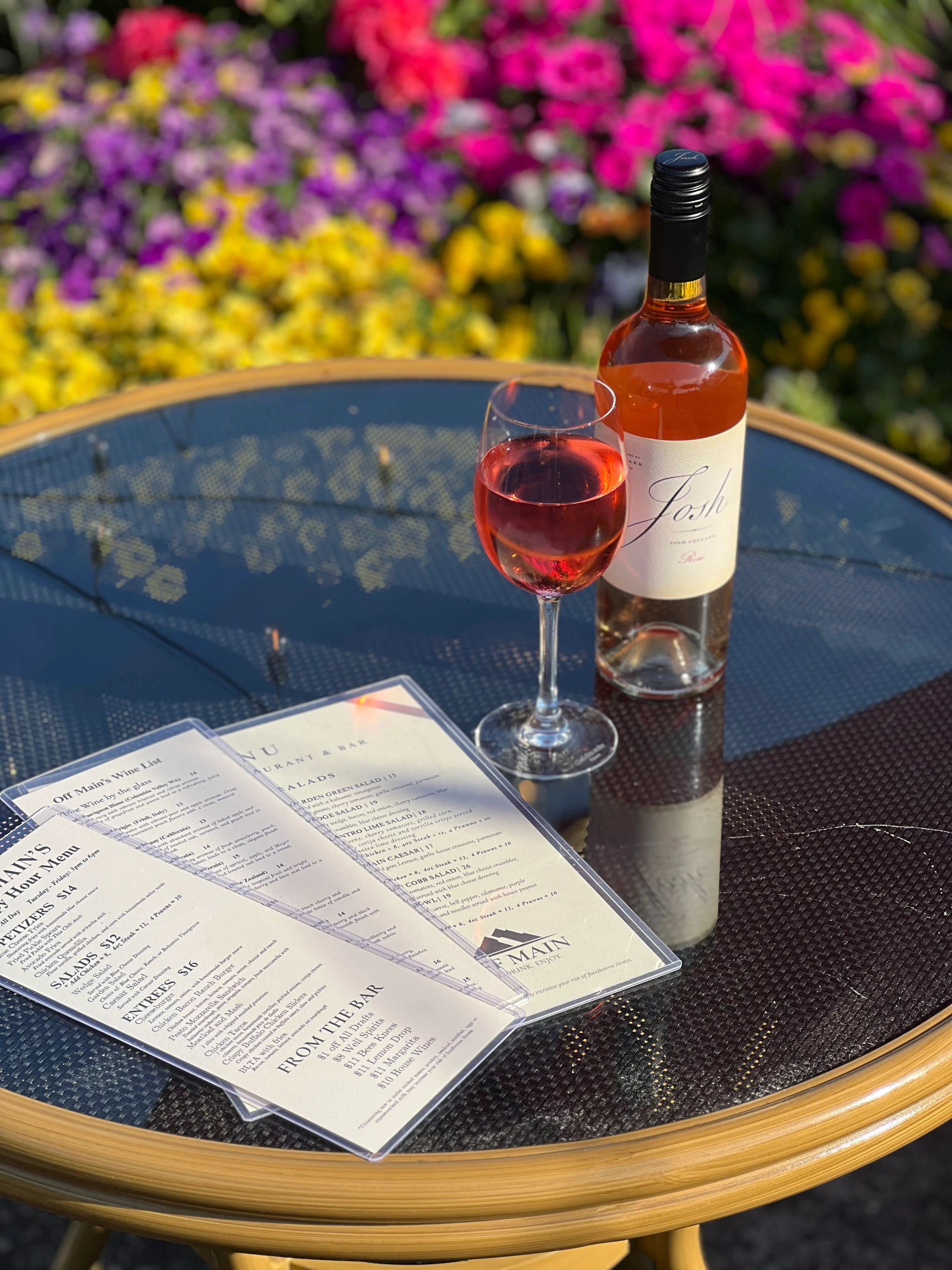 An outdoor lunch scene with a plate of loaded fries, tortilla chips, and a small bowl of dip, alongside a bottle of wine.
