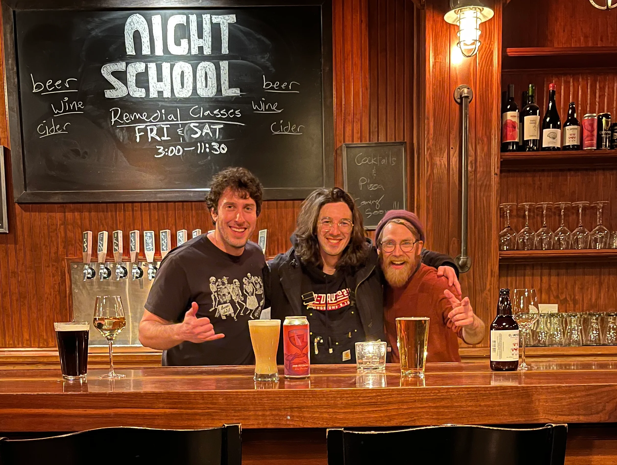 Johnny, Wes, and Nate behind the bar under "Night School" on the chalk board.