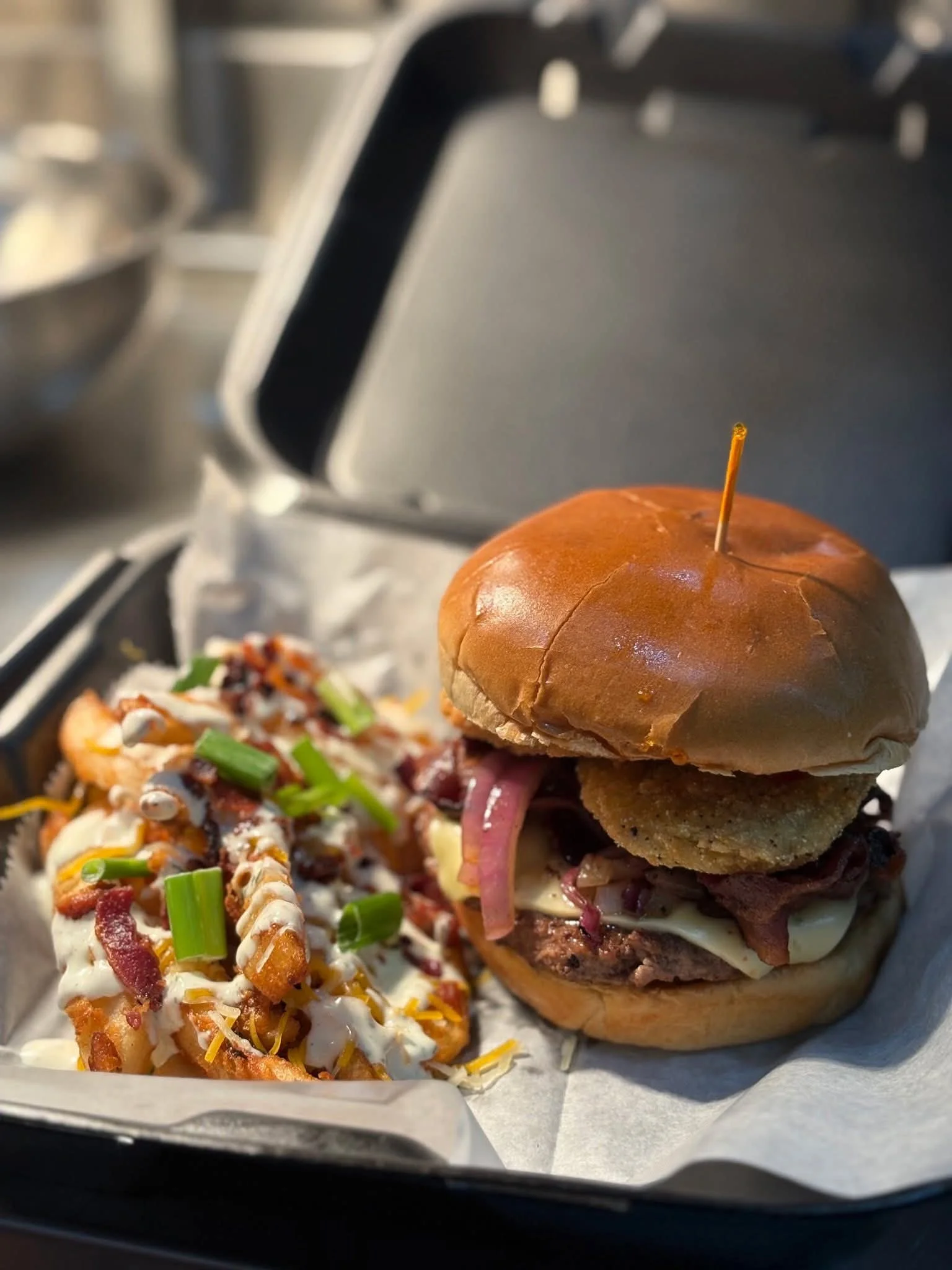 Loaded BBQ burger with fries in a takeout box
