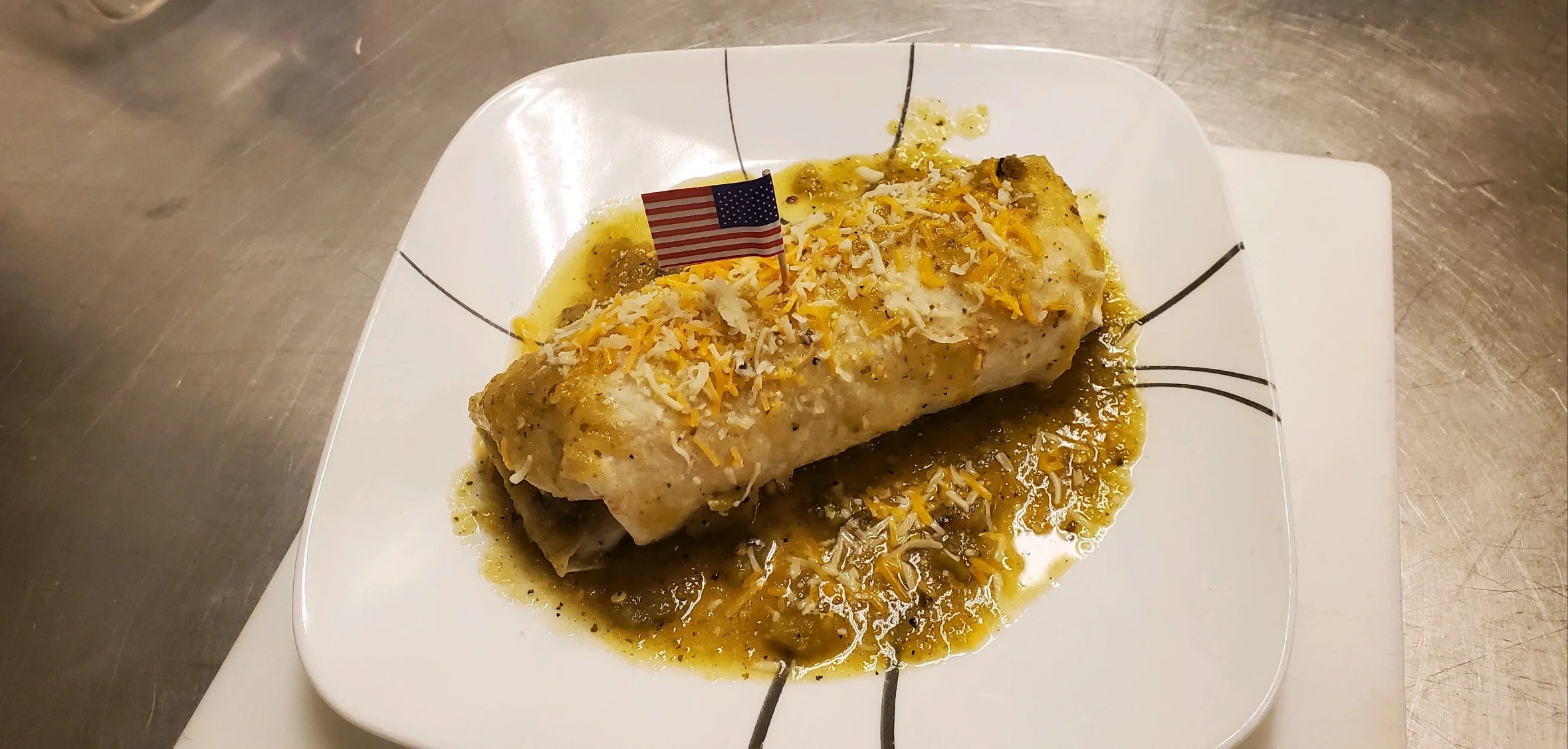 A burrito topped with cheese and a small American flag on a plate.