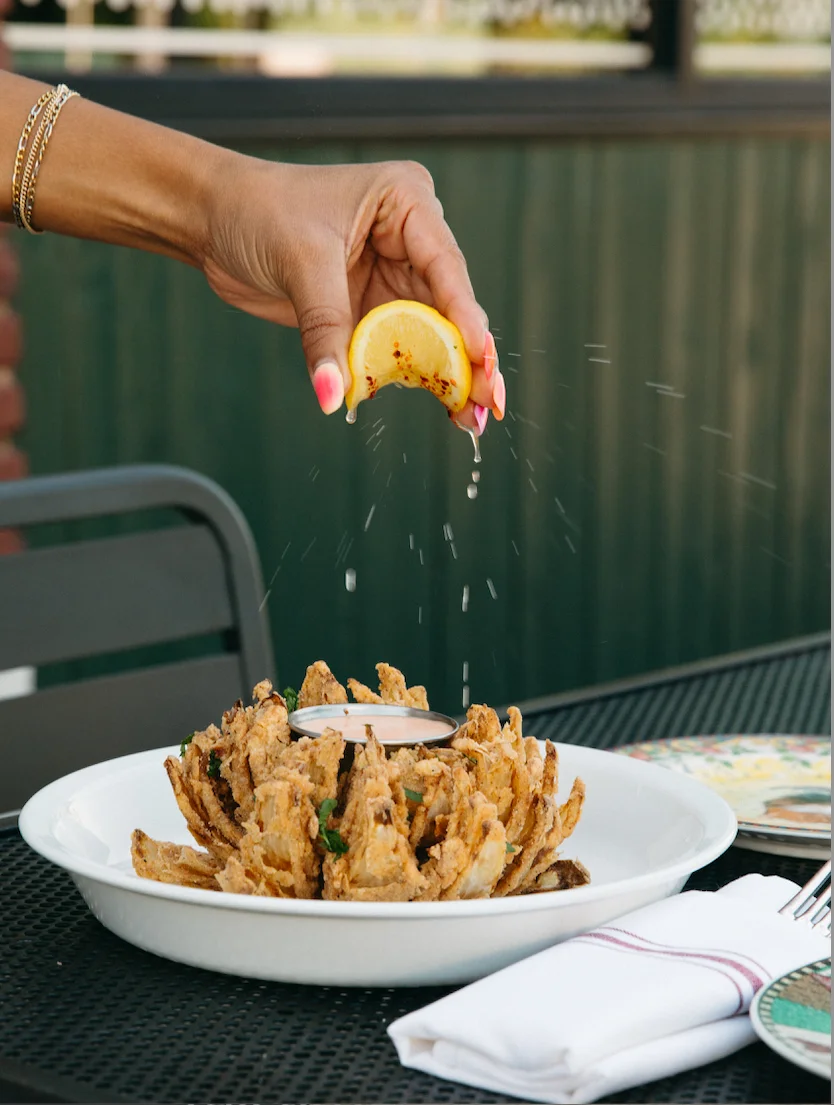 A hand squeezing a lemon over a large serving of crispy fried onion petals, ready to enhance its flavor.