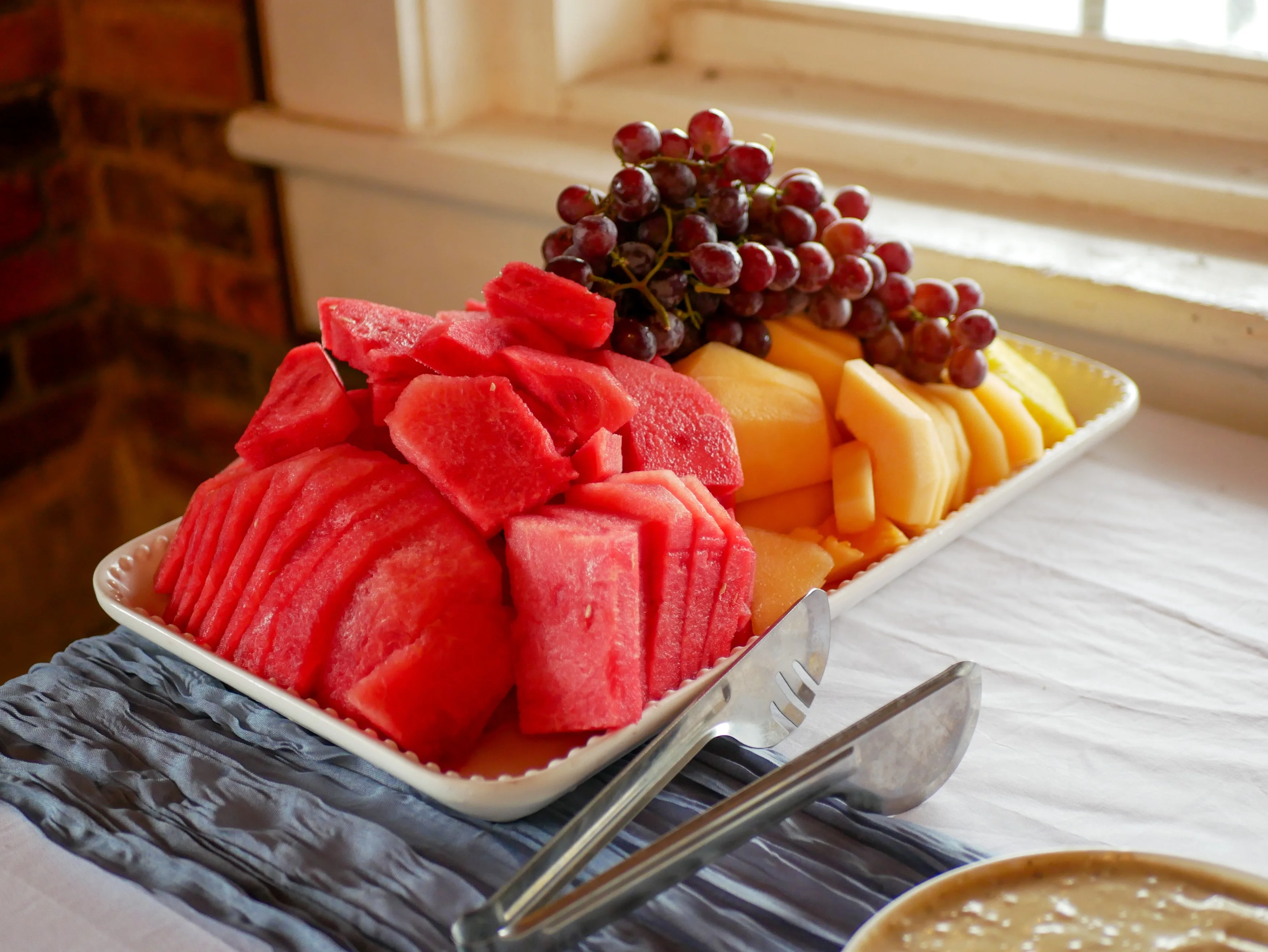 A platter of assorted fresh fruits including sliced watermelon, cantaloupe, and grapes.