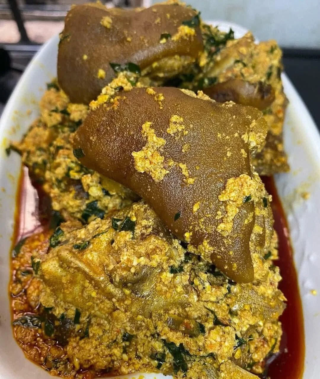 A dish featuring pig's feet covered in a rich, yellow sauce with green herbs, served in a white bowl.