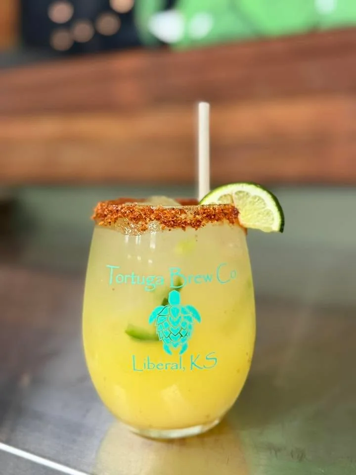 A refreshing cocktail served in a glass with a rim of chili salt and topped with a lime wedge. The drink appears to contain ice and fresh ingredients.