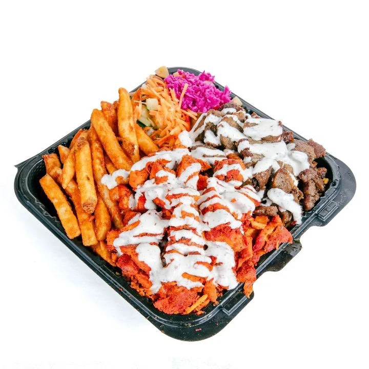 A generous platter featuring a mix of sliced chicken and beef, accompanied by crispy fries and colorful slaw. The dish is drizzled with a white sauce and garnished with green toppings.