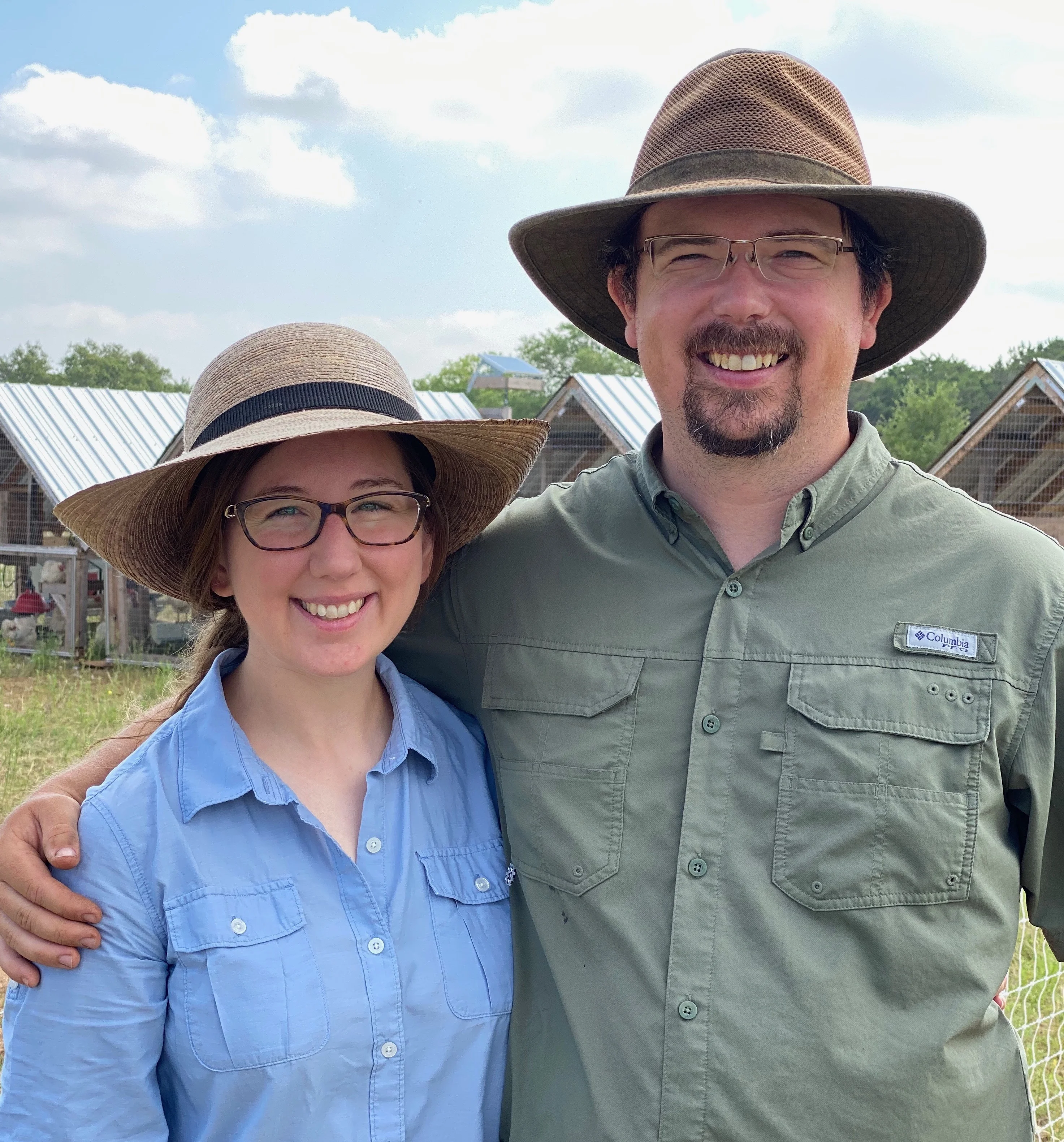 Couple in hats at a farm with chicken coops in the background