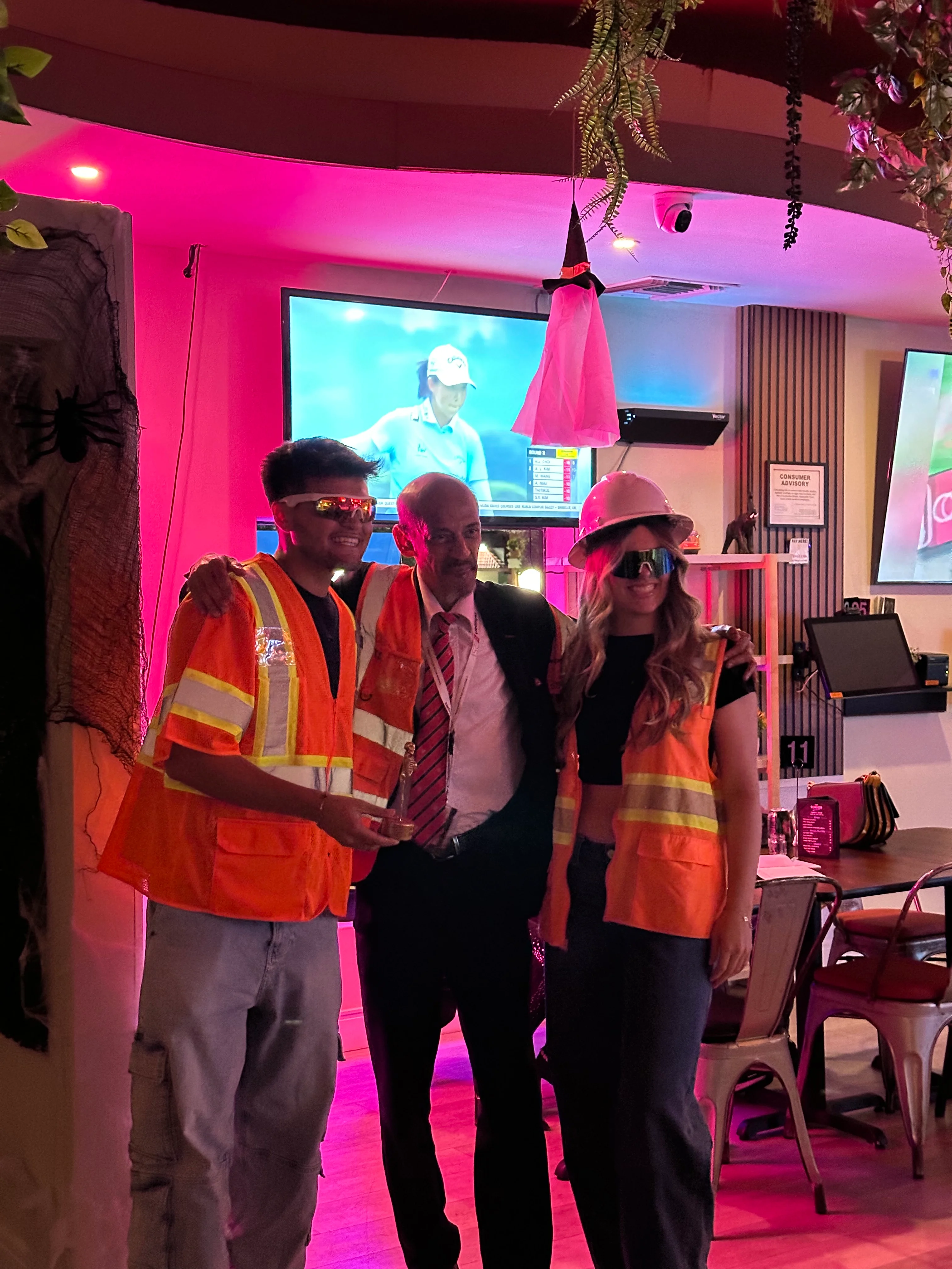 Three people in safety vests posing in a vibrant restaurant setting