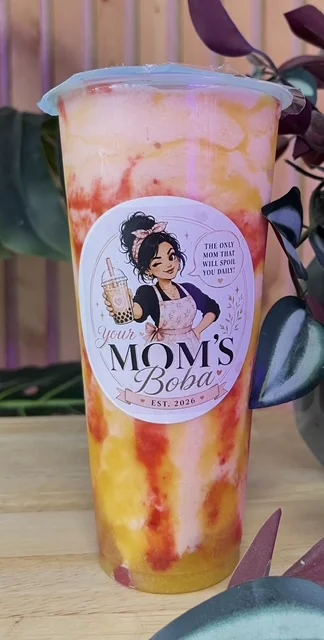 A colorful boba drink with layers of orange and pink hues, topped with a clear lid. The cup features a playful logo for a boba shop.