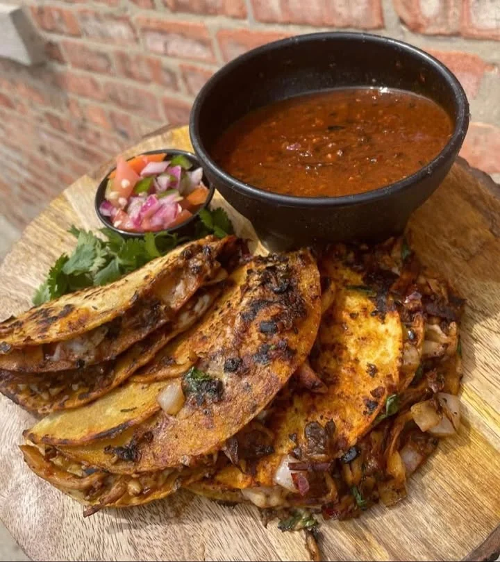 A plate of three tacos filled with seasoned meat and garnished with fresh herbs, showcasing crispy and lightly charred tortillas.