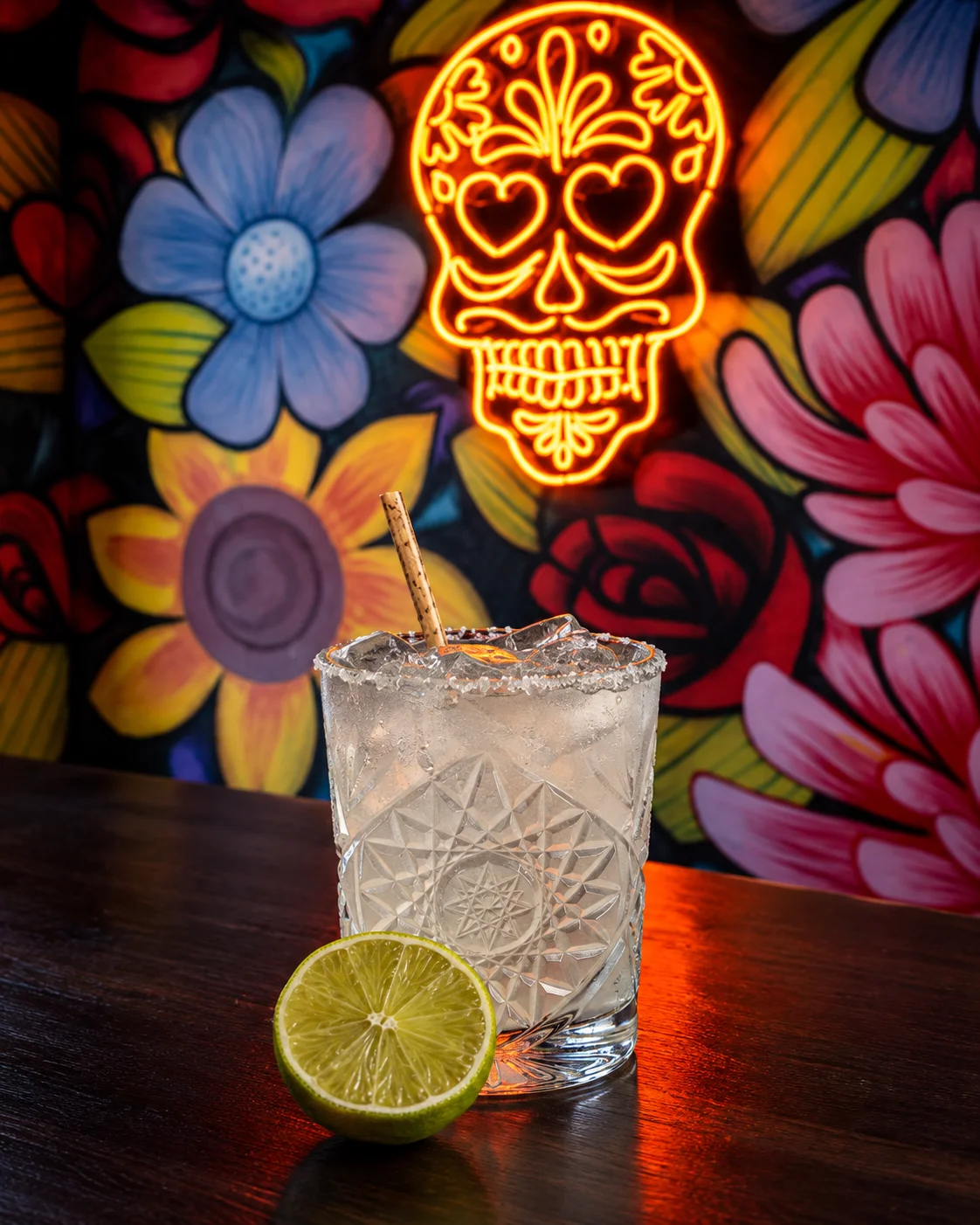 Refreshing cocktail with lime on a wooden table against vibrant floral mural