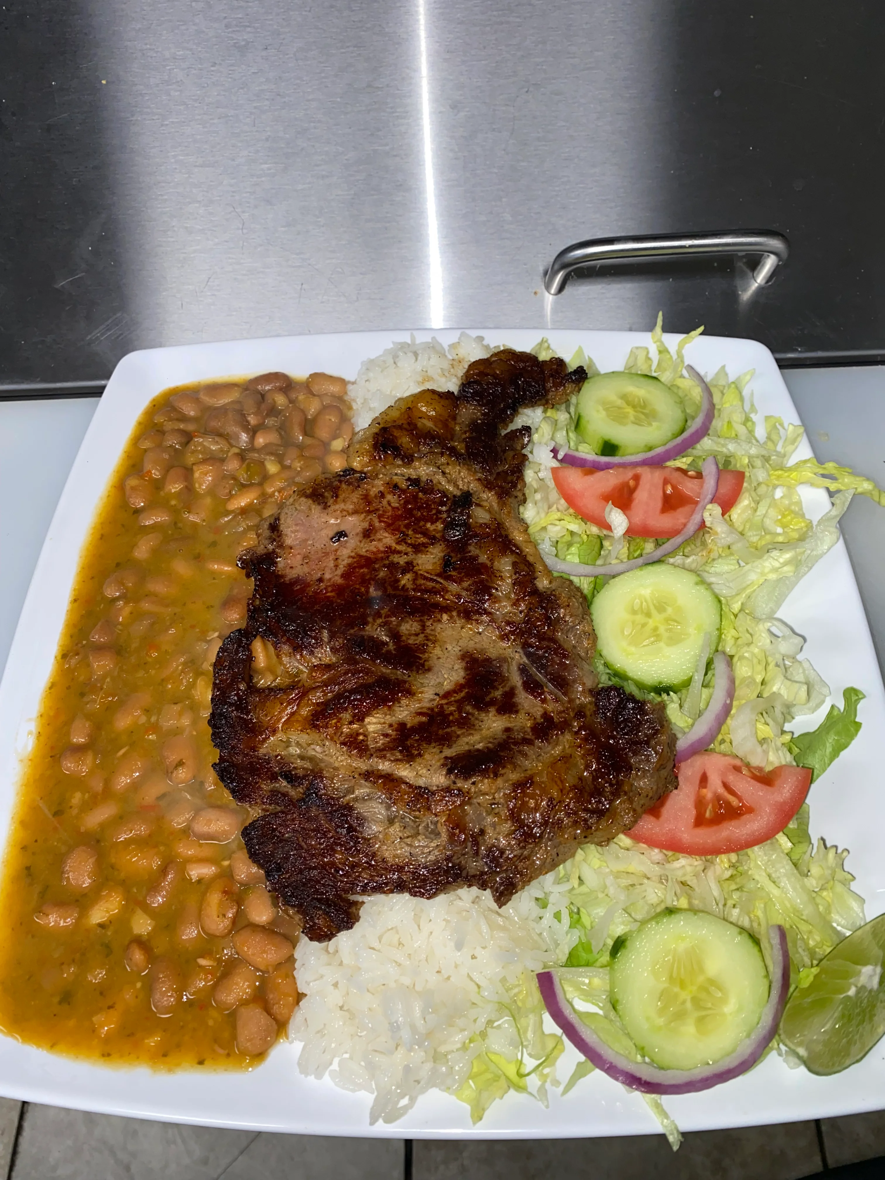 A plate featuring grilled steak served with a side of rice, beans, and a fresh salad including lettuce, tomatoes, and cucumbers.