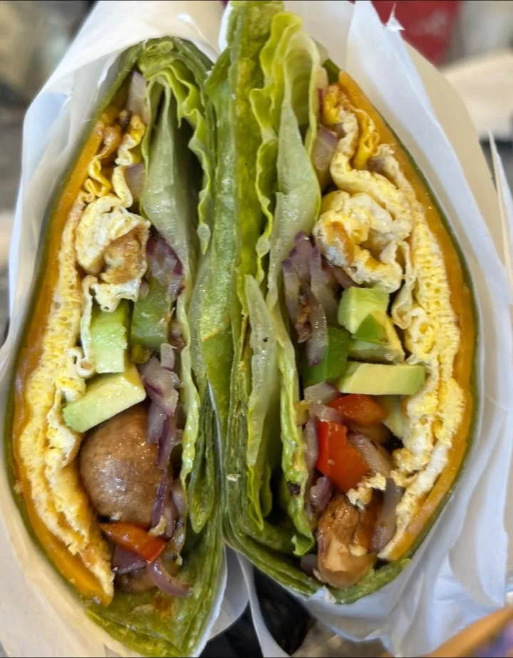 A cross-section of a wrap filled with greens, vegetables, and eggs, neatly arranged in a paper wrapper.