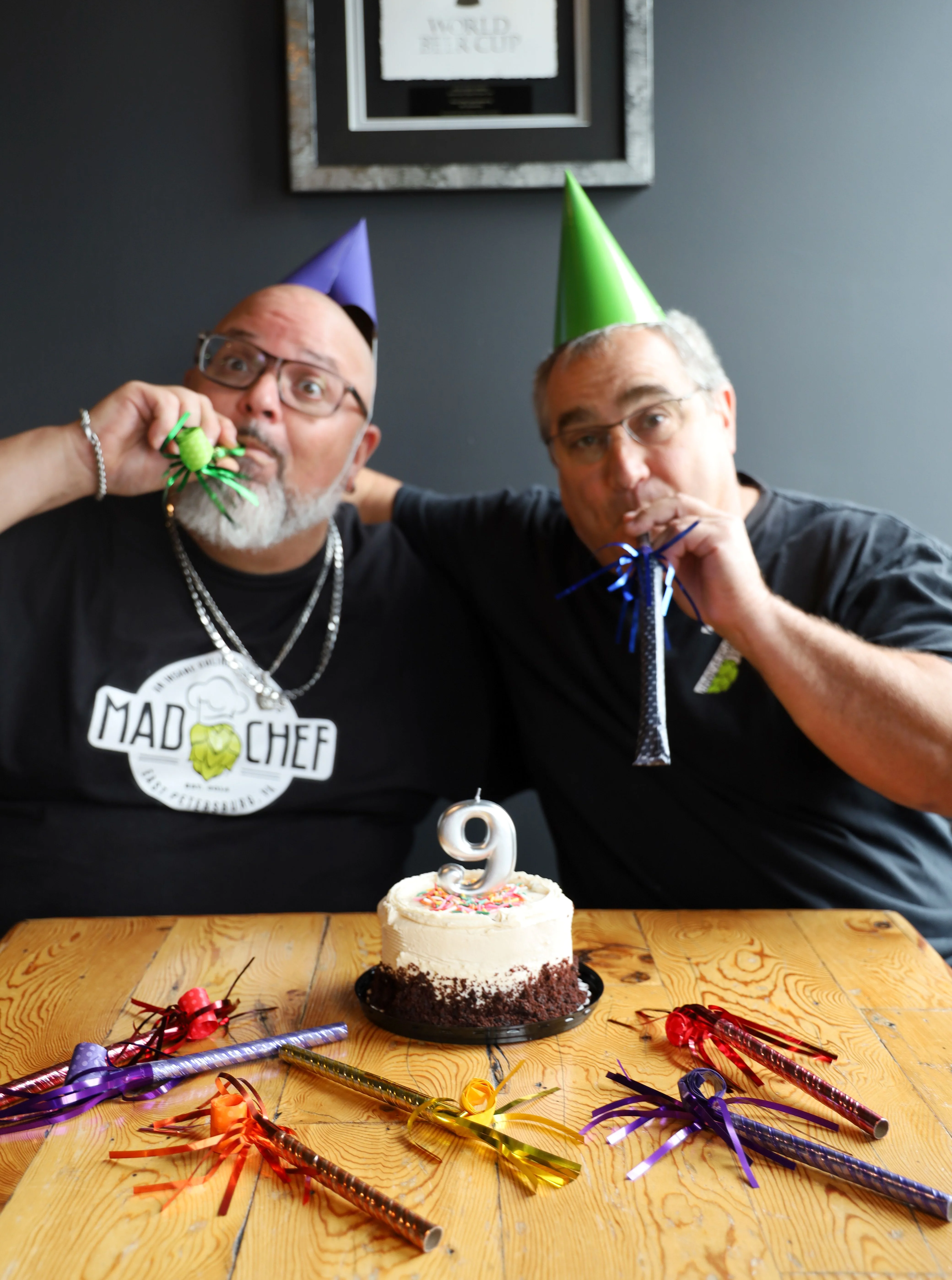 Two chefs posing by a large hop cone logo in a brewery