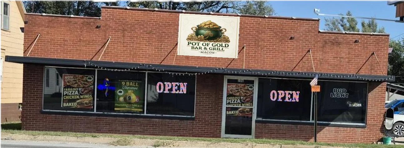 A brick building featuring a bar and games, with large windows displaying signs advertising pizza and chicken wings. The establishment is open and marked with neon lights.
