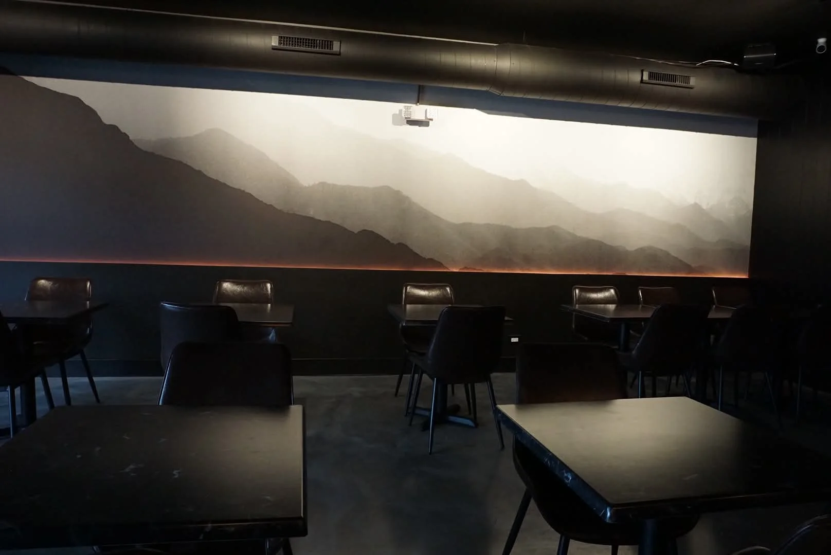 Modern restaurant interior with mountain mural and dark furniture.