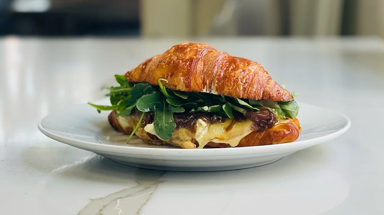 French breakfast sandwich with brie and caramelized onions on a buttery croissant
