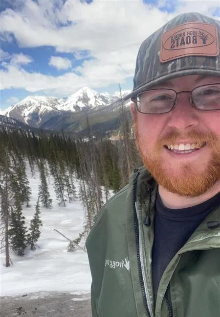 Person smiling in snowy mountain landscape with pine trees