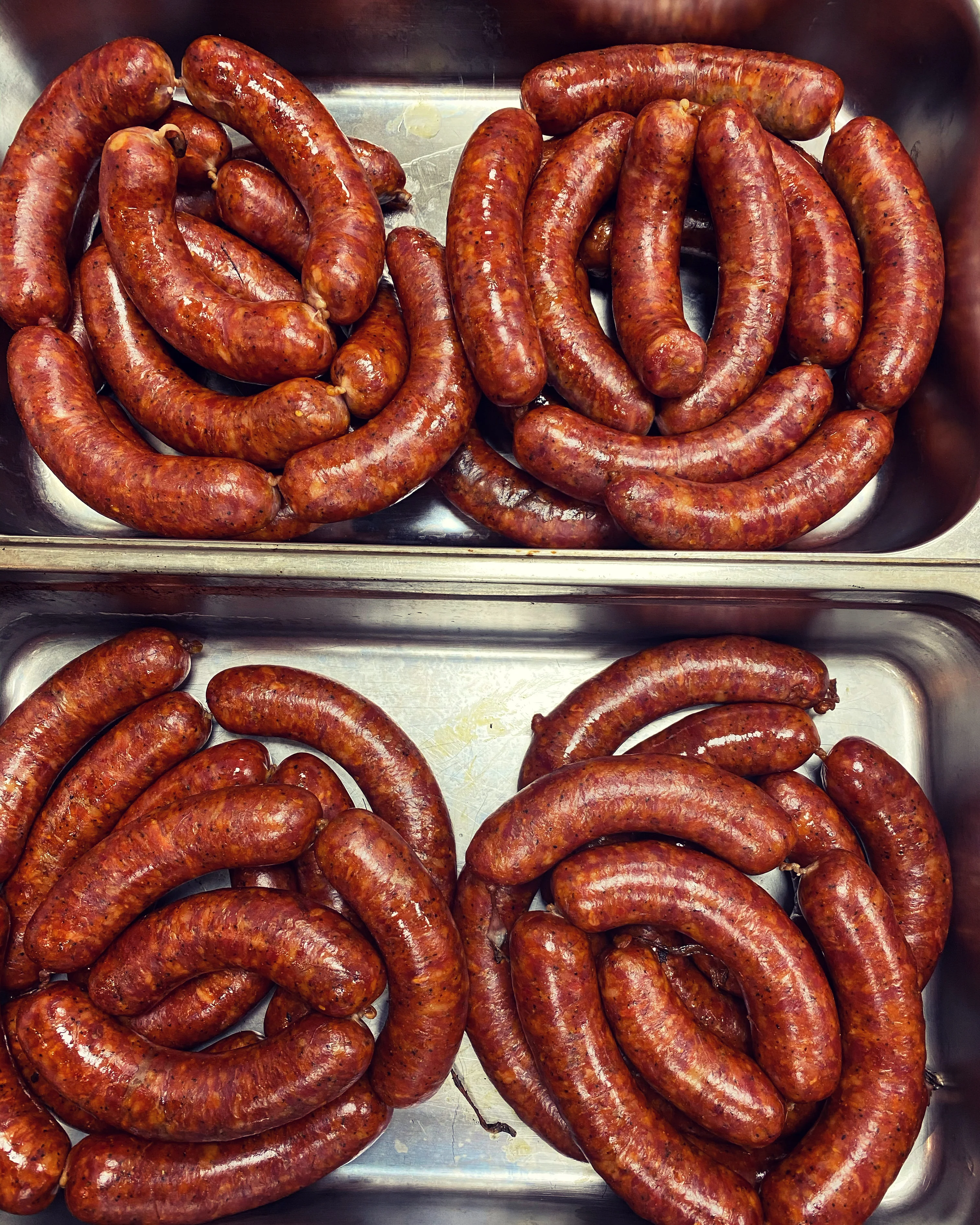 A close-up of freshly made sausages arranged in trays, showcasing their rich, reddish-brown color and presented in an organized manner.