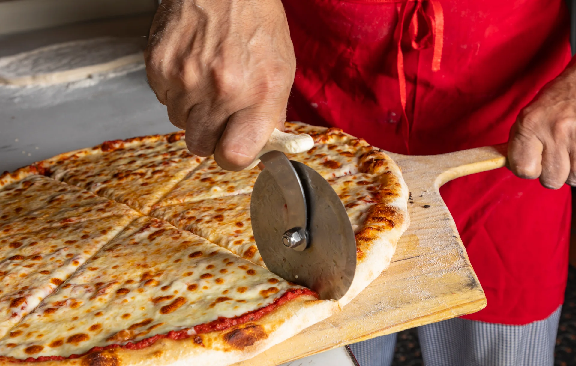 Hand cutting a Margherita pizza with a pizza cutter