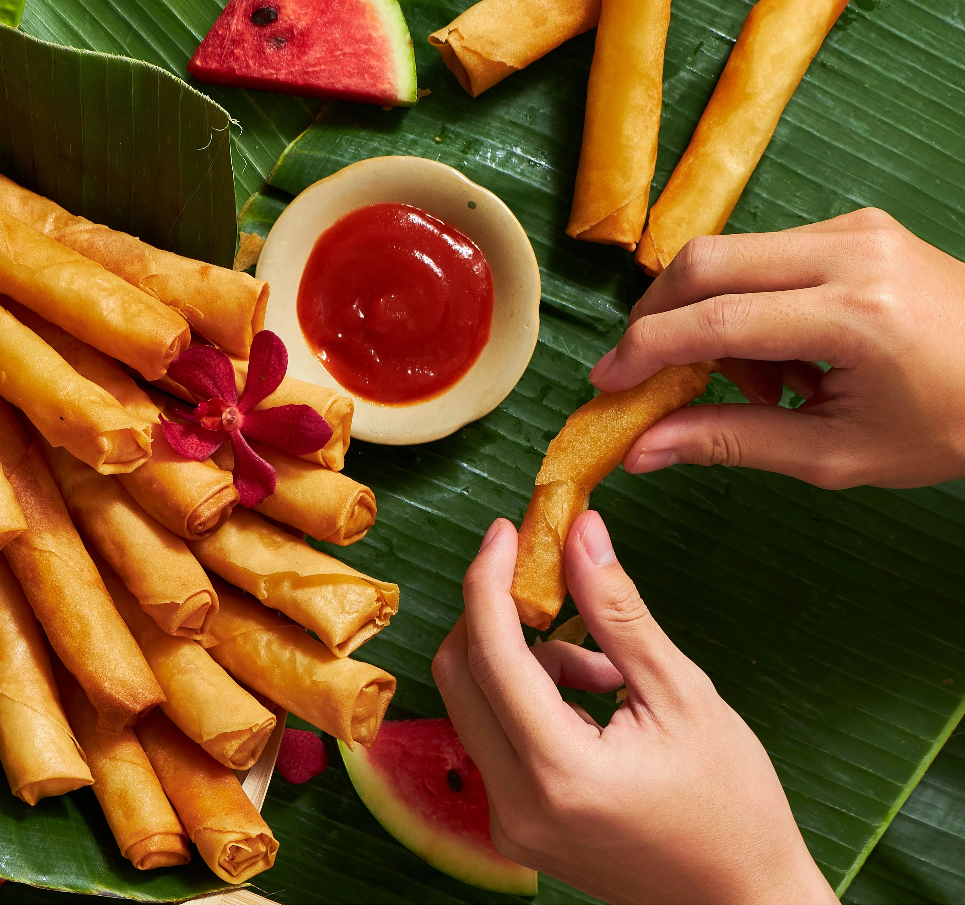 Crispy Filipino lumpia served with dipping sauce on banana leaves