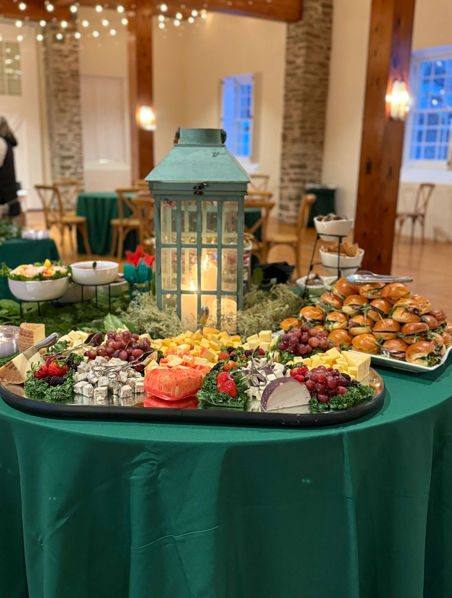 Round table with beautifully displayed catered food, including sliders, cheeses, and charcuterie