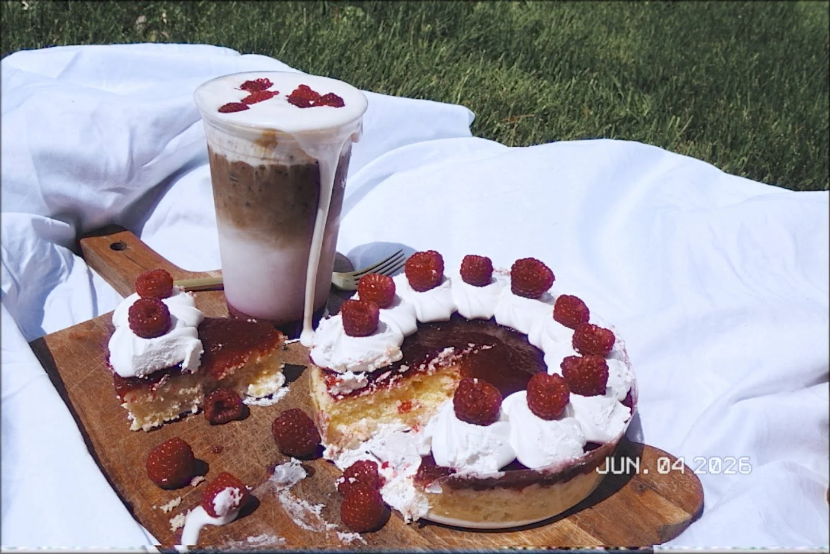 Raspberry cheesecake with whipped cream and iced coffee in a picnic setting