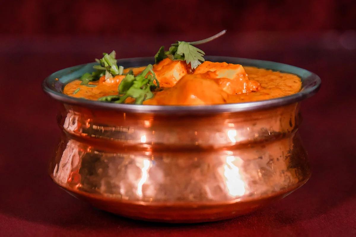 A delicious bowl of classic Chicken Tikka Masala from Mint Indian Restaurant, featuring a rich, creamy tomato sauce and a garnish of fresh cilantro.