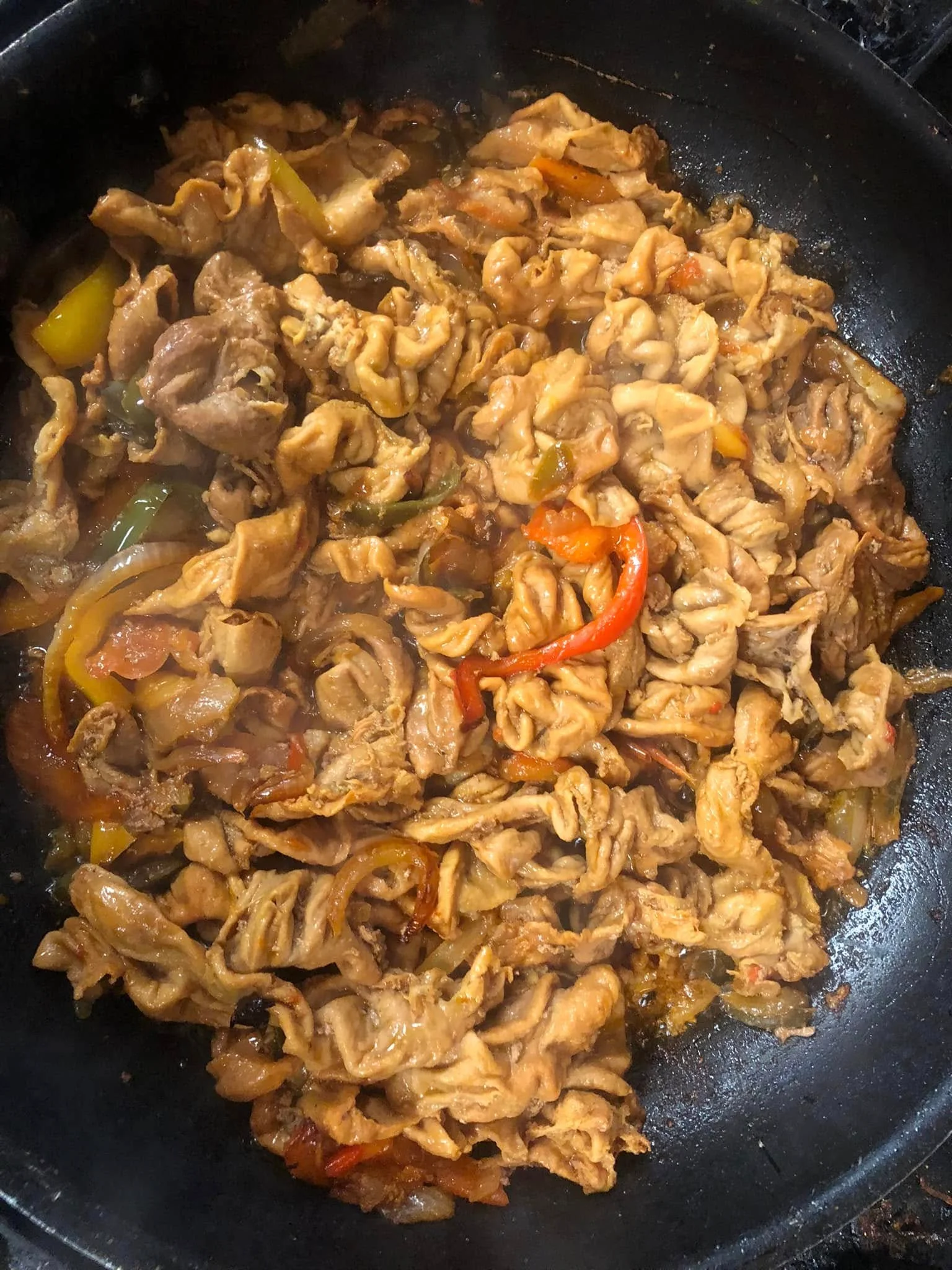 A pan of simmered chitterlings (pig intestines) cooked with onions, peppers, and seasoning in a rich brown gravy.