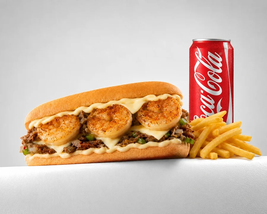 A sandwich filled with grilled shrimp, beef, and cheese, accompanied by a can of cola and fries.