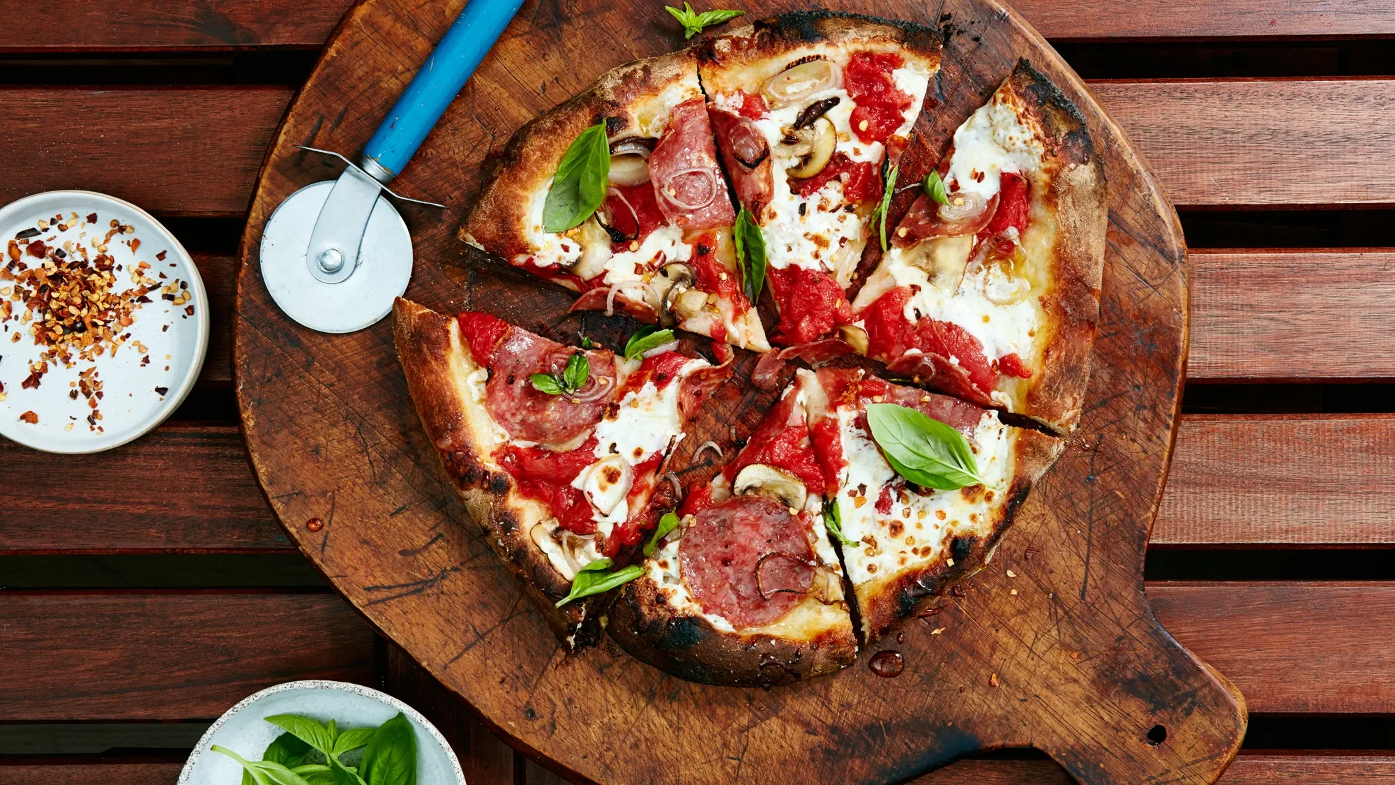 A freshly baked pizza sliced into pieces, topped with pepperoni, cheese, and basil, served on a wooden cutting board.