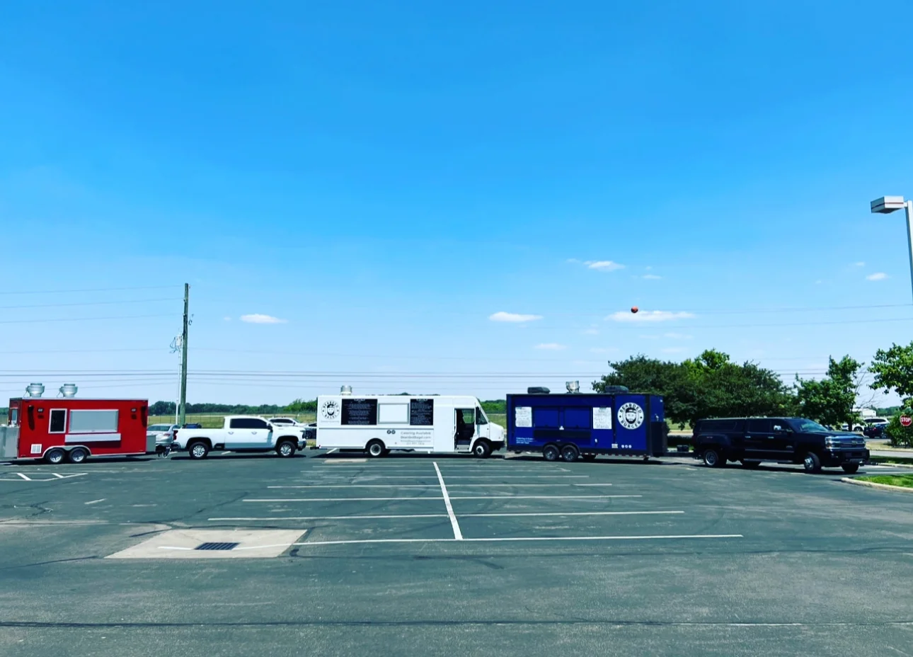 Food trucks lined up in a parking lot under a clear blue sky