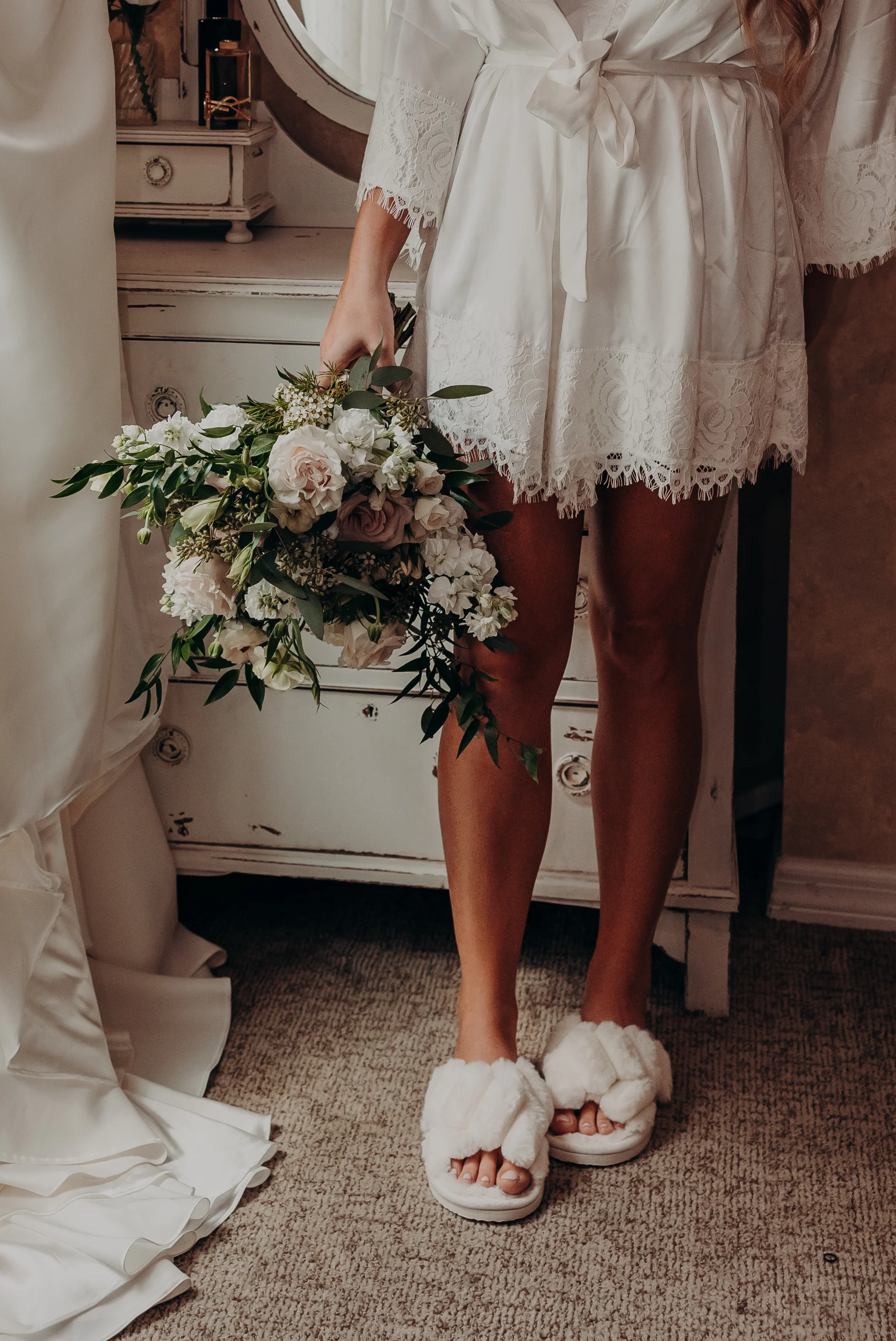 Bride in white robe holding a floral bouquet before wedding